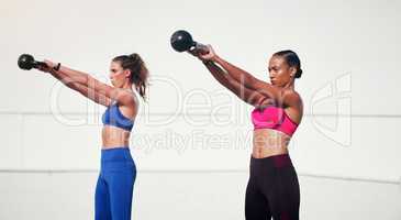 Every swing counts. two attractive young sportswomen working out with kettle bells outdoors.