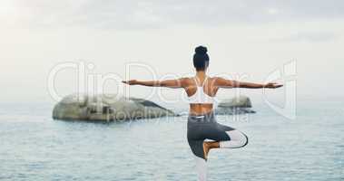 Trusting my balance. Rearview shot of an unrecognizable woman standing and doing yoga alone by the ocean during an overcast day.