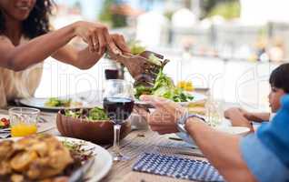 More greens for me please. an unrecognizable woman dishing up salad on her husbands plate while enjoying a meal with family outdoors.