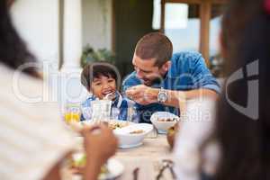 His appetite is growing bigger by the day. a father feeding his young son during a meal with family outdoors.