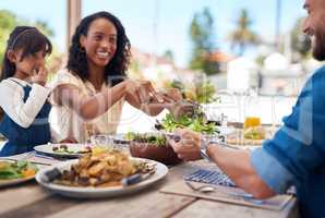 She always makes sure we maintain a healthy diet. a beautiful young woman dishing up salad on her husbands plate while enjoying a meal with family outdoors.