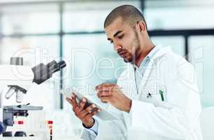 Serious male scientist working on a tablet reviewing an online phd publication in a lab. Laboratory worker updating health data for a science journal. Medical professional document clinical trial