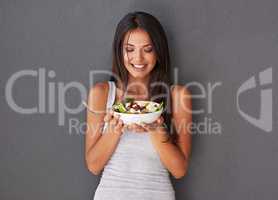 Healthy young female eating her fresh food salad bowl. Smiling beautiful woman holding and enjoying eating her clean green diet dish of vegetables as part of her vegan wellness lifestyle