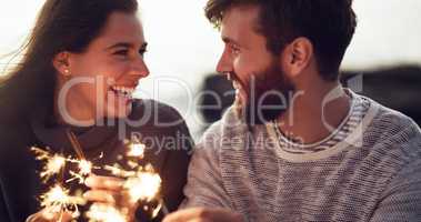 The sparkle in your eyes tells me that you love me. a young couple holding sparklers on the beach.