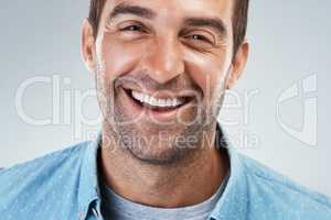 Now thats a good smile. Portrait of a cheerful young man smiling brightly while standing against a grey background.