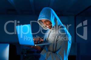 Firewall breached. a young male hacker smiling while using a laptop in the dark.