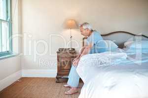I wonder what I should do today. a senior man sitting alone on the edge of his bed and looking contemplative at home.