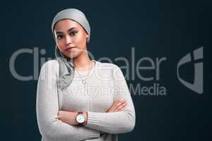 I am proud to be muslim. an attractive young woman wearing a headscarf and standing with her arms folded against a black background.