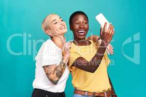 Best friends make the best memories. Studio shot of two young women taking selfies together against a turquoise background.