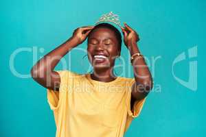 Princess Try queen. Studio shot of a young woman putting a crown her head against a turquoise background.