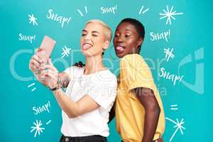 When life gets serious take lots of silly selfies. Studio shot of two young women taking selfies together against a turquoise background.