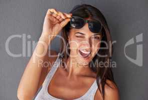 Beautiful, attractive and flirty portrait of a young woman. Isolated stylish sexy, funny and joyful, funky girl winking while lifting up her sunglasses against a copy space background.