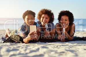 Lets remember this moment forever. an attractive young trio of women laying down on the beach and taking selfies together during the day.