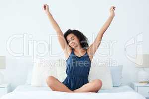 The early bird catches the worm. an attractive young woman sitting up in bed and stretching with her arms raised in the morning.