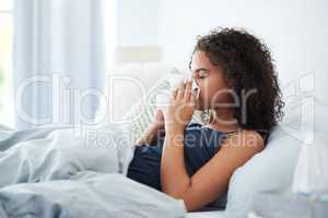 Oh no Ive got a cold. an attractive young woman feeling sick and blowing her nose while in bed in the morning.