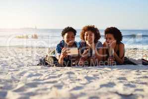 Selfie time. an attractive young trio of women laying down on the beach and taking selfies together during the day.