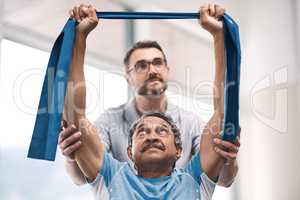 Were getting fitter by the day together. a senior man exercising with a resistance band during a rehabilitation session with his physiotherapist.