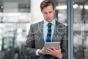 Checking my to-do list. a handsome young businessman standing alone in his office and using a tablet.