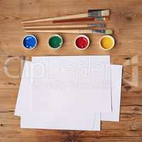 Art, painting and creative supplies on a wooden desk with paper from above. Paintbrushes, colors and still life containers ready to create artwork or an artistic design in studio with copy space