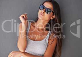 Funky, confident and beautiful woman wearing sunglasses and looking cool against a grey wall background. Face of an edgy, stunning and happy young female feeling good with attractive or trendy style