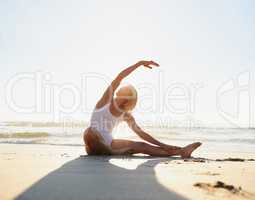 Stretch and hold. Full length shot of an attractive young woman doing a yoga stretch early in the morning on the beach.