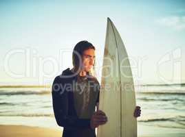 Im out to chase some waves. a young man standing with a surfboard at the beach.