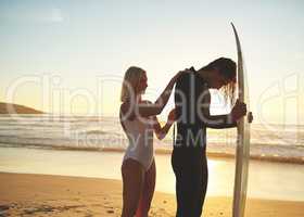 Let me help you get ready babe. a young couple zipping up his wetsuit before going surfing at sunset.