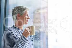 You grow wiser in thought as the years go by. an attractive mature businesswoman drinking coffee while looking out of her office window.
