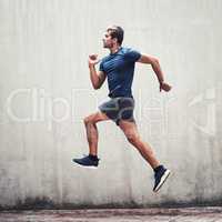 Skip over every hurdle until you reach your goal. a sporty young man running against a grey wall outdoors.