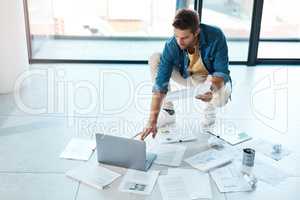 Making his dreams work through thorough planning. a young businessman brainstorming with a laptop and paperwork on a floor in an office.