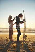 Almost zipped up. Full length shot of a young couple zipping up his wetsuit before going surfing at sunset.