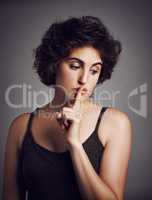 I better keep quiet about this. Studio shot of an attractive young woman with her finger over her lips against a grey background.
