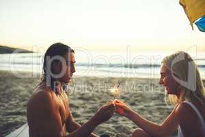 I love sparklers. a happy young couple having fun and lighting sparklers while on a date on the beach at sunset.