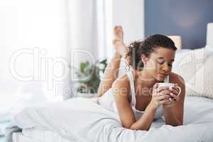 Start your day with a cup of comfort. an attractive young woman enjoying a cup of coffee while relaxing on her bed at home.
