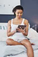 So much to catch up to. an attractive young woman using her digital tablet while sitting on her bed at home.