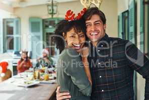 Spend your Christmas with the people you love. Portrait of a happy young couple celebrating Christmas together over lunch with friends and family in the background.