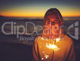 Dont let anyone dim your light from within. Portrait of a young woman holding a sparkler at the beach at night.