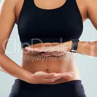 Maintain a balance between regular exercise and healthy eating. Studio shot of an unrecognizable sporty woman framing her stomach with her hands against a grey background.