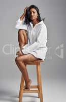 Shes owning her throne. Portrait of a beautiful young woman sitting on a stool against a grey background.