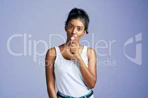 I love sweet things. Studio portrait of a beautiful young woman sucking on a lollipop against a purple background.