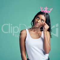 Royal thoughts. Studio shot of a beautiful young woman posing with a prop crown against a green background.