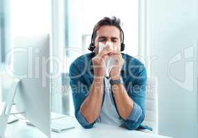 I hope no one else catches this flu Im having. a male call centre agent blowing his nose with a tissue in his office.