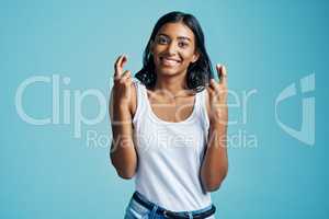 Heres hoping. Studio portrait of a beautiful young woman crossing her fingers against a blue background.