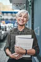 Everyday is a new day to learn something new. Portrait of a cheerful mature businesswoman carrying books and paperwork while out in the city.