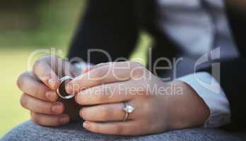 So much sadness in a single ring. Closeup shot of an unrecognizable businesswoman holding a wedding ring while sitting in a public park.