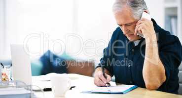 Yes, Im dotting down your every request. a mature businessman writing a few notes down while answering a phone call in his office.