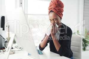 She cant afford to be sick right now. an attractive young businesswoman blowing her nose while working at her desk in the office.