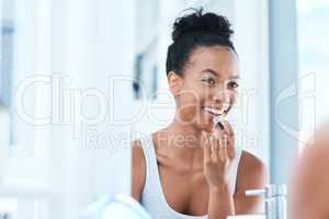 These lips are ready to spread some positivity. a young woman applying lipstick in her bathroom mirror.