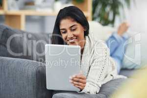 Catch up on the currents while you relax. an attractive young woman using her digital tablet while relaxing on he couch at home.