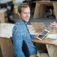 Confident marketing manager browsing the internet on a digital tablet in an office. Handsome and happy professional researching creative ideas to promote and advertise a startup on social media